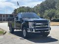 A black 2022 Ford F-350 SD pickup truck with chrome accents and a utility bed is parked in a lot with its headlights on and a small flag attached to the cab roof