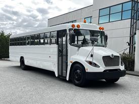 A 2015 Spartan School Bus with a white exterior and multiple orange lights on the roof stands parked with its door open