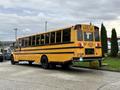 A yellow 2014 Freightliner B2 school bus with black stripes and multiple windows on the side is parked with the back facing the viewer