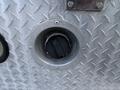 A circular fuel access port with a black cap on a metal diamond plate surface