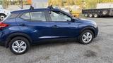 A blue 2019 Nissan Kicks parked on gravel showcasing its compact design and five-door layout with a side view that highlights the wheels and door handles