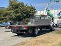 A 2004 Ford F-750 flatbed truck with a wooden bed and a black metallic frame parked on a paved surface