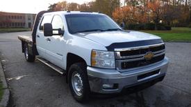 A white 2014 Chevrolet Silverado 3500HD with a flatbed, chrome grille, and black accents parked on a concrete surface