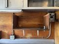 A wooden shelf with two metal supports and a panel with electrical outlets and a circuit breaker in a food truck interior