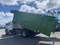 A 1997 Freightliner FL70 dump truck with its bed raised, displaying a green dump body positioned at an angle