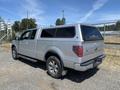 A silver 2014 Ford F-150 pickup truck with a truck cap parked on gravel with a shiny exterior and alloy wheels