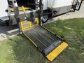 A wheelchair lift extended from a 2020 Chevrolet Express featuring a metal mesh platform with yellow accents and two yellow handles for operation