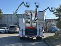 A white 2006 Freightliner M2 106 bucket truck with two raised aerial work platforms attached to the rear and a warning sign stating FREQUENT STOPS