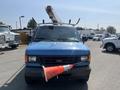 A blue 2005 Ford Econoline van with a utility rack on the roof and an orange traffic cone hanging from the front grill