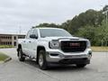 A white 2016 GMC Sierra 1500 truck is parked with a chrome grille and black accents showcasing its rugged design and spacious cab