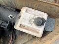 A weathered plastic fluid reservoir with a circular cap showing signs of wear and damage mounted on machinery