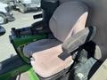 A gray upholstered seat of a 2016 John Deere 1585 Terrain Cut mower with armrests and control levers beside it
