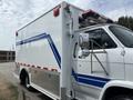 A 1994 GMC Vandura 3500 with a white body and blue stripes featuring an emergency light on the roof and chrome side mirrors
