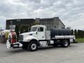 A 2016 Peterbilt 348 truck with a black tank on the back and a large red hose reel mounted on the side