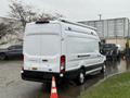 A white 2023 Ford Transit van parked with a sloped rear and a roof rack
