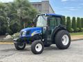 A blue 2009 New Holland T4020 tractor with a cab and large wheels stands prominently in the foreground