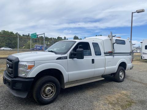 A 2014 Ford F-350 SD in white with a utility bed and ladder rack parked on gravel with an angled view showing the driver's side