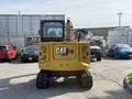 A yellow 2022 Caterpillar 306 excavator with a cab and tracks viewed from the rear