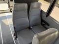 Two gray upholstered seats in the foreground of a bus interior, featuring vertical stripes and seatbelts