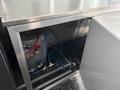 Interior view of a 2020 Freightliner MT45 showing metal shelves and plumbing with various colored hoses connected to a water heater and distribution system
