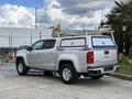 A silver 2018 Chevrolet Colorado pickup truck with a white camper shell mounted in the bed and chrome wheels