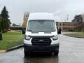 A white 2020 Ford Transit van is parked facing the camera with its headlights on and water droplets on the windshield