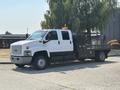 A white 2005 GMC C7500 Topkick truck with a flatbed and toolboxes on the side parked on a paved area