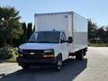 A 2024 Chevrolet Express cargo van, white with a boxy shape and large rear storage area, parked and facing forward in a well-lit setting