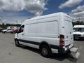 A white 2016 Mercedes-Benz Sprinter van with a gray stripe on the side is parked with its rear visible, featuring a side door and alloy wheels