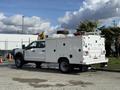 A white 2024 Ford F-550 truck with a utility body featuring compartments and equipment on the back and a spare tire mounted on the roof