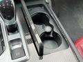 A cup holder in a 2016 Maserati Ghibli's center console featuring a sleek design with carbon fiber texture and a button labeled with a cup symbol