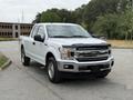 A white 2018 Ford F-150 pickup truck facing forward with chrome accents on the grille and headlights parked on asphalt