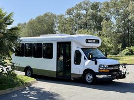 A 2020 Chevrolet Express bus with a white body and black accents featuring a front display reading SAFE BUS