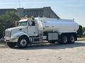 A 2008 Peterbilt 340 truck with a white tank trailer and visible orange lights on the roof parked on a concrete surface