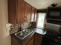 A kitchen area in a 2013 Outdoor Wind River featuring wooden cabinets a double sink and appliances including a microwave and stove
