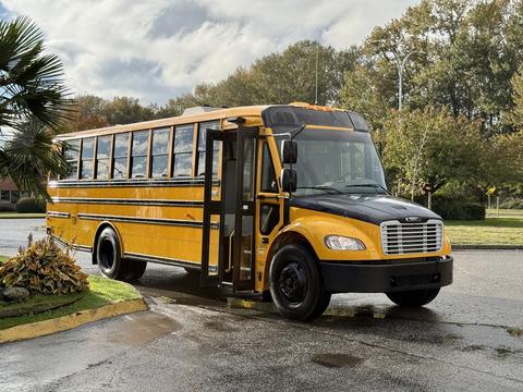 A yellow 2022 Freightliner B2 school bus with a black front bumper and open door parked on a road