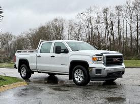 A white 2015 GMC Sierra 1500 pickup truck parked on a wet surface with a double cab and chrome accents