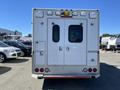 A rear view of a white 2013 Chevrolet Express ambulance with double doors and emergency lights on the roof