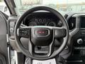 Steering wheel of a 2022 GMC Sierra 1500 featuring the GMC logo with various control buttons and a dashboard with gauges in the background