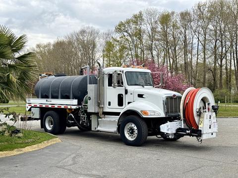 A white 2016 Peterbilt 348 truck with a large black tank in the back and a hose reel mounted on the front side
