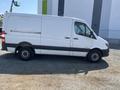 A 2016 Mercedes-Benz Sprinter van in white with a black stripe along the bottom parked on gravel
