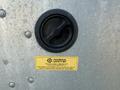 Close-up of a black circular cap with a safety label attached showing technical information and a warning regarding liquid level gauge requirements