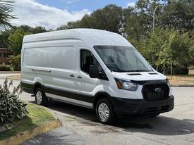 A 2021 Ford Transit van in white with a black grille parked at an angle showcasing its front and side features
