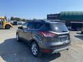 A 2016 Ford Escape parked at a lot, featuring a gray exterior and chrome wheels with a rear view showing the hatchback design