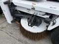 Close-up of a 2012 Global M4 street sweeper with a large circular sweeping brush and hydraulic components visible
