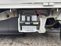 A black and gray battery mounted under the chassis of a 2008 Suzuki Carry with visible connections and a label attached