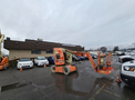 A 2009 JLG E300AJP aerial lift in orange and gray with a platform extending upward parked in a lot among vehicles