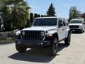 A white 2021 Jeep Wrangler Rubicon with a bold grille and off-road tires is parked with its headlights on