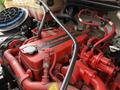 Close-up of a red Cummins engine with various hoses and components visible in an engine compartment of a vehicle.