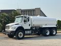A 2016 Freightliner M2 106 truck with a white tanker body and multiple axles is parked with its cab facing the viewer